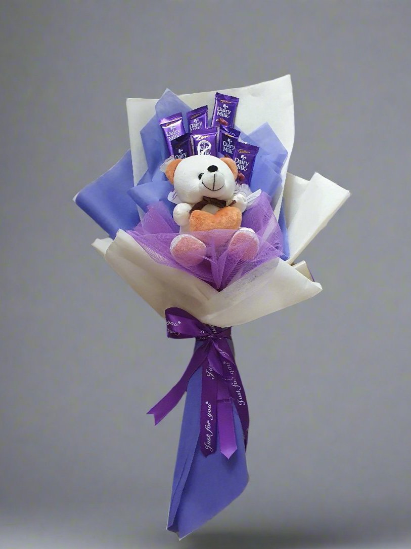 Surprise someone with a beautiful gift: 7 Dairy Milk chocolates, a teddy bear, wrapped in white-blue paper and purple ribbon.