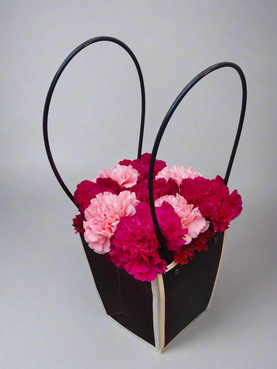 A black box surrounded by vibrant red and pink carnations, blending mystery with romantic elegance in a striking floral display.