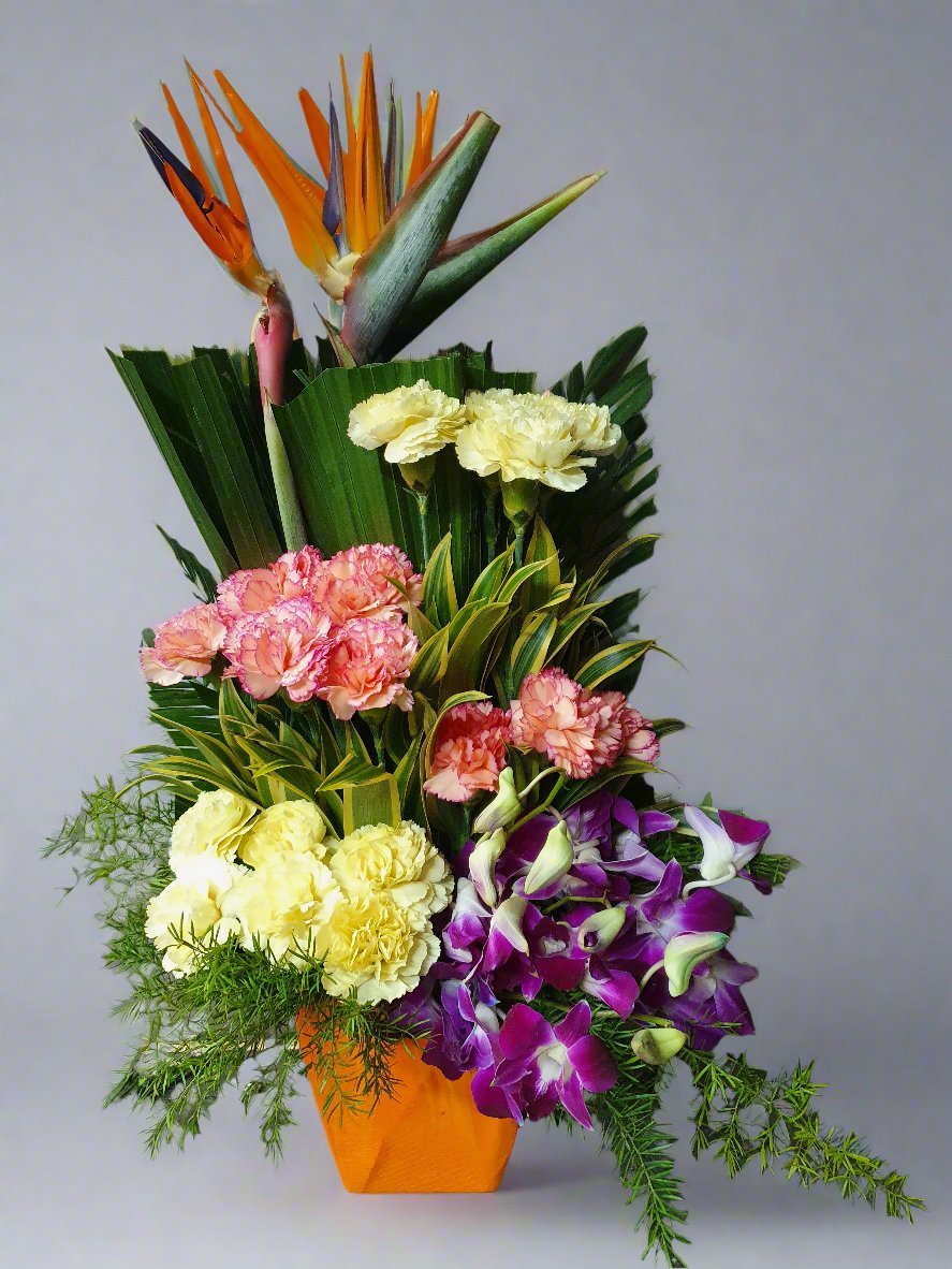 A vibrant mix of pink, yellow carnations and purple bloom with lush green leaves in a beautiful yellow pot, perfect for brightening any space.