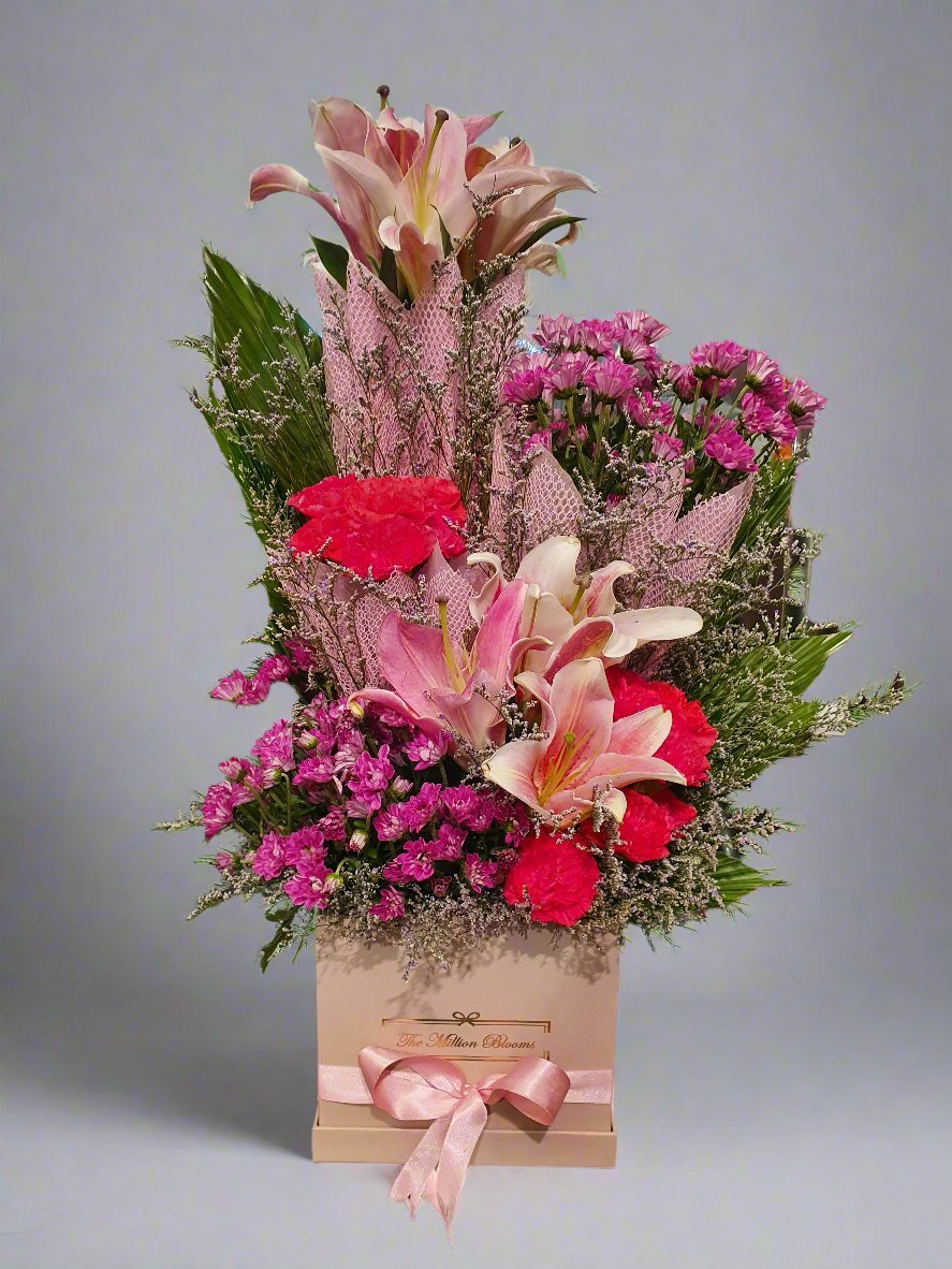 A stunning blend of soft pink daisies and delicate pink lilies shines against lush green foliage, creating a serene, eye-catching floral masterpiece.