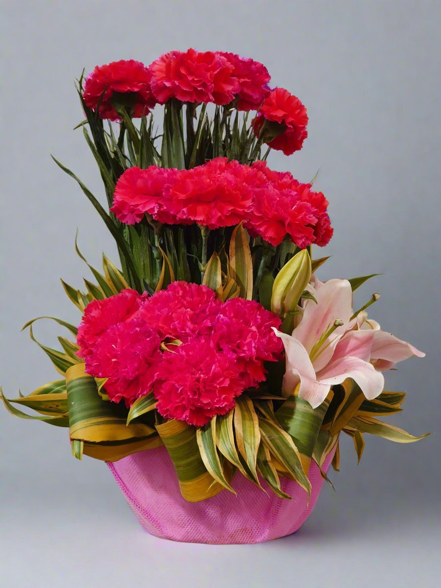 Discover an elegant floral arrangement in a stylish pink pot, featuring red carnations, pink lilies, and lush green leaves. Perfect for décor.