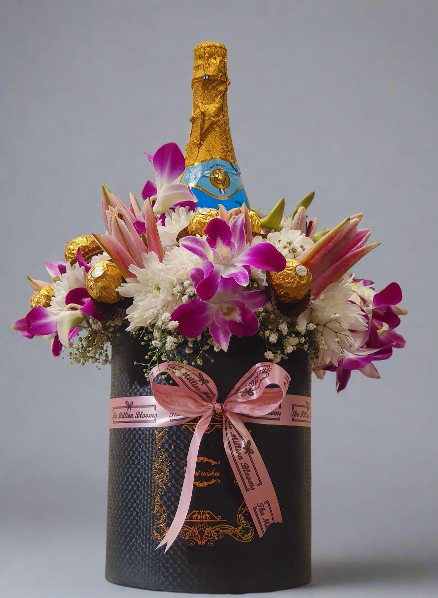 Celebrate in style with a bottle of champagne, vibrant pink lilies, white daisies, orchids, and golden Ferrero Rocher chocolates.