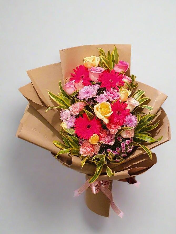 A vibrant bouquet of yellow roses, pink carnations, daisies, and roses offers a stunning blend of warmth, elegance, and charm for any occasion.