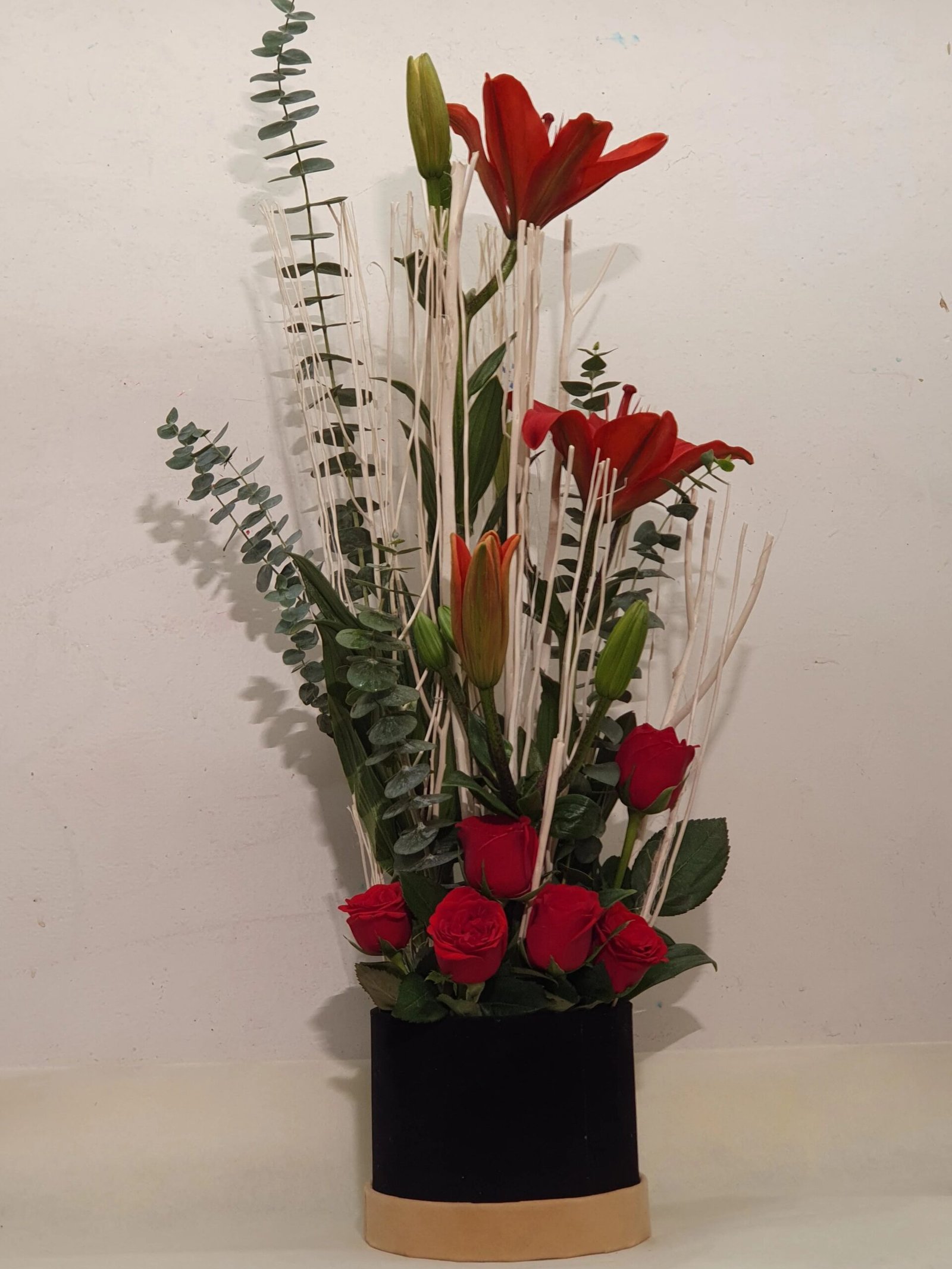 A bold black box with red roses,red lilies and green leaves, creating a striking, sophisticated floral arrangement perfect for any occasion.