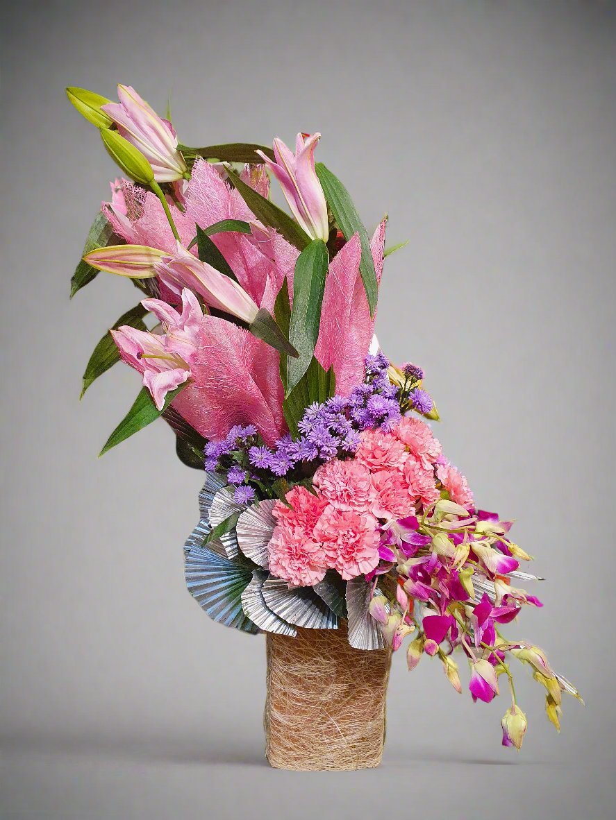 Discover the beauty of a delicate arrangement featuring pink lilies, carnations, and orchids, each showcasing its unique charm and elegance.