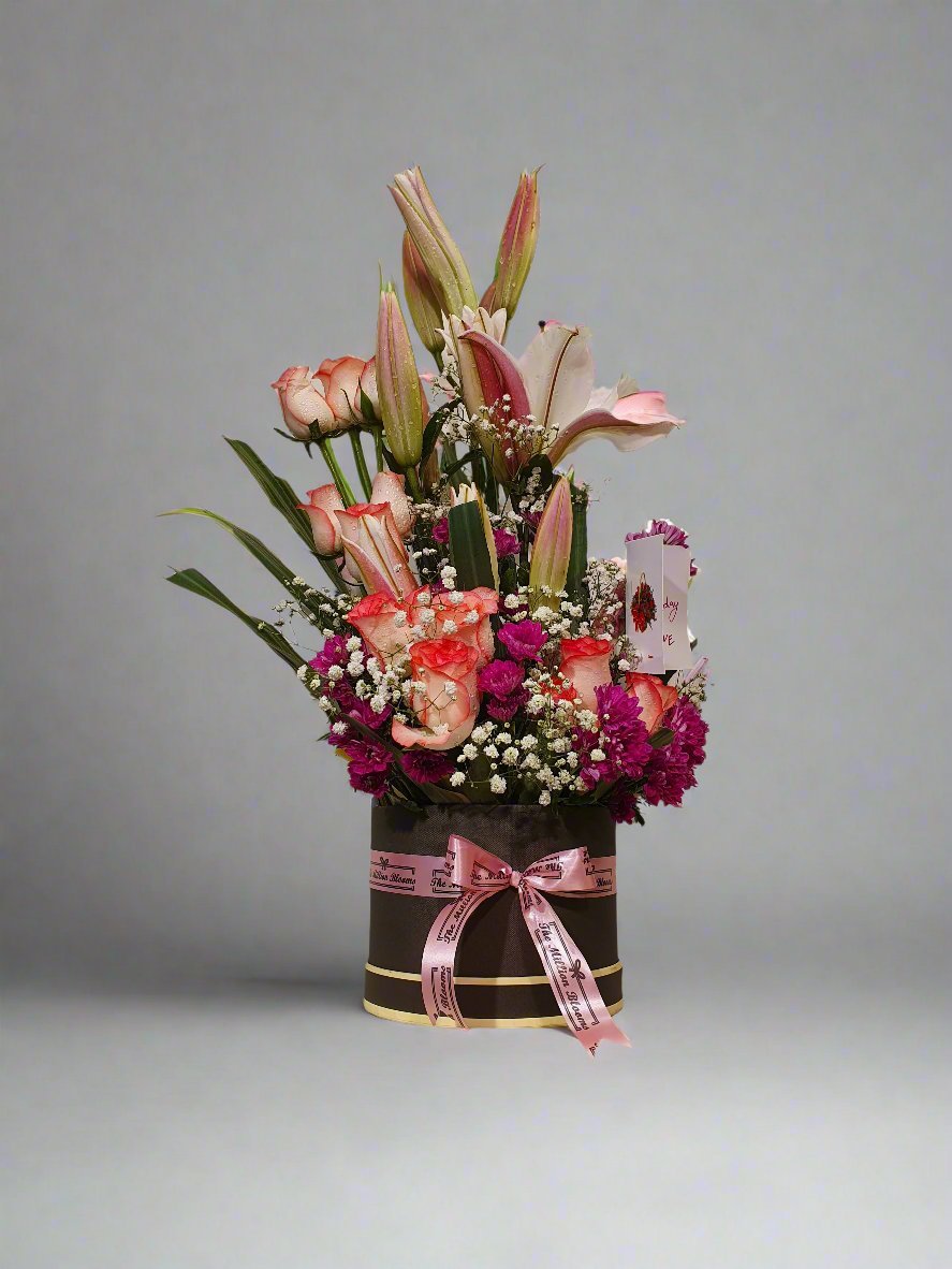 A stunning mix of red roses, purple carnation, pink lilies, and white flowers in a chic brown box. Perfect for any occasion.